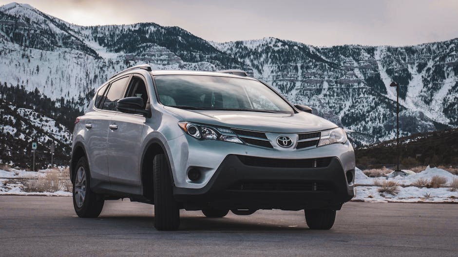 A silver SUV is parked in front of stunning snow-covered mountains during daytime.